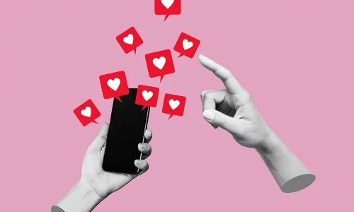 Mano sujetando un móvil con notificaciones de corazones saliendo de la pantalla, representando la gestión de redes sociales y el aumento de interacción.