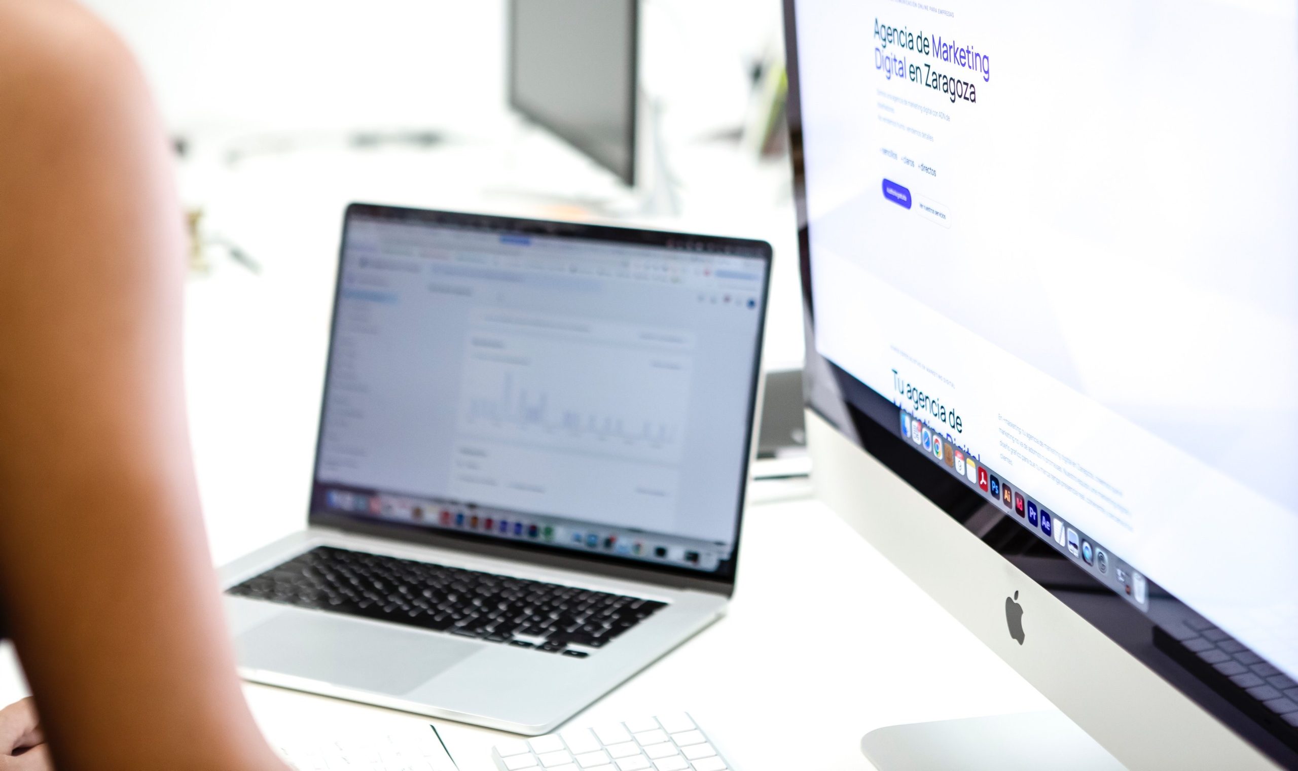 Puesto de trabajo de +másketing con un portátil y un iMac mostrando la web de la agencia